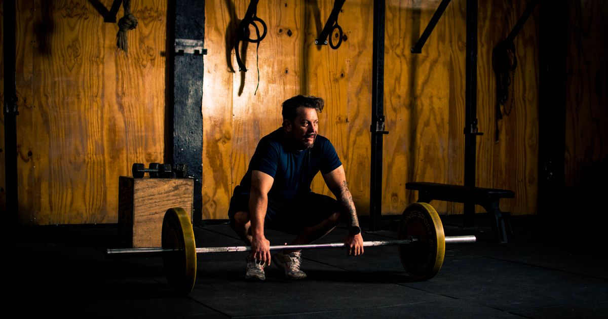 Man set up to row a loaded barbell in a dimly lit gym, the T-bar row hinge position