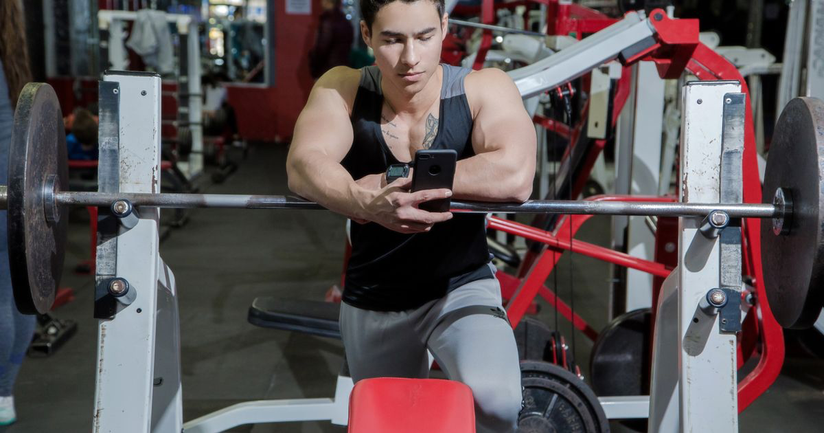 Lifter leaning on a barbell using his phone to track gym progress between sets