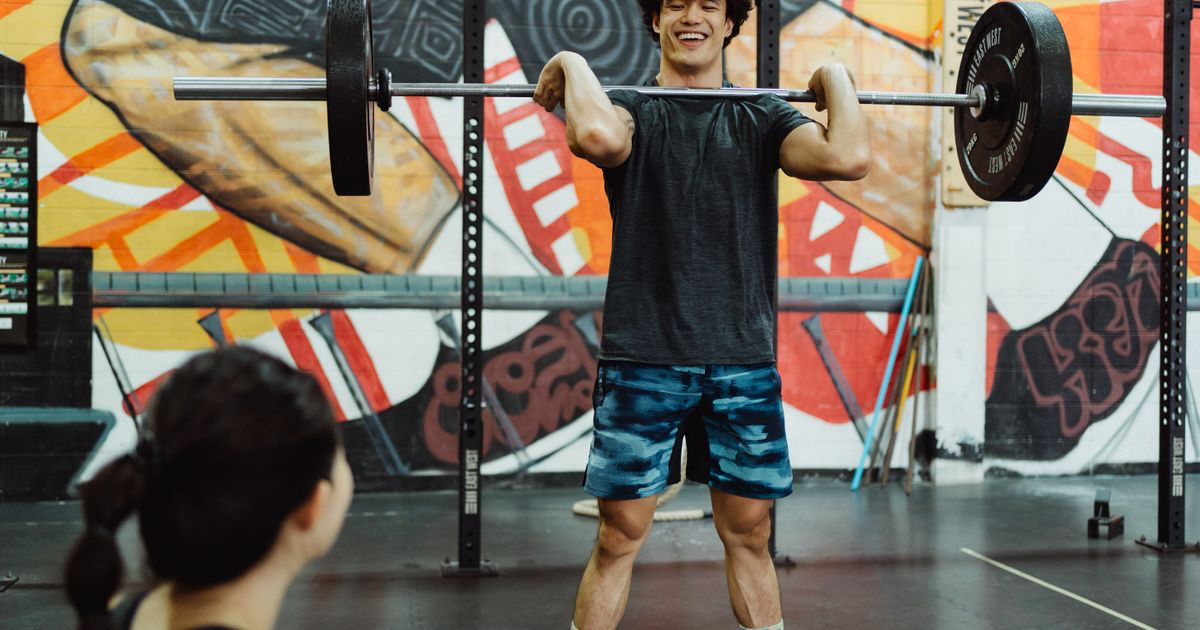 Man holding a loaded barbell across his shoulders, illustrating the squat day of a 3 day full body workout plan