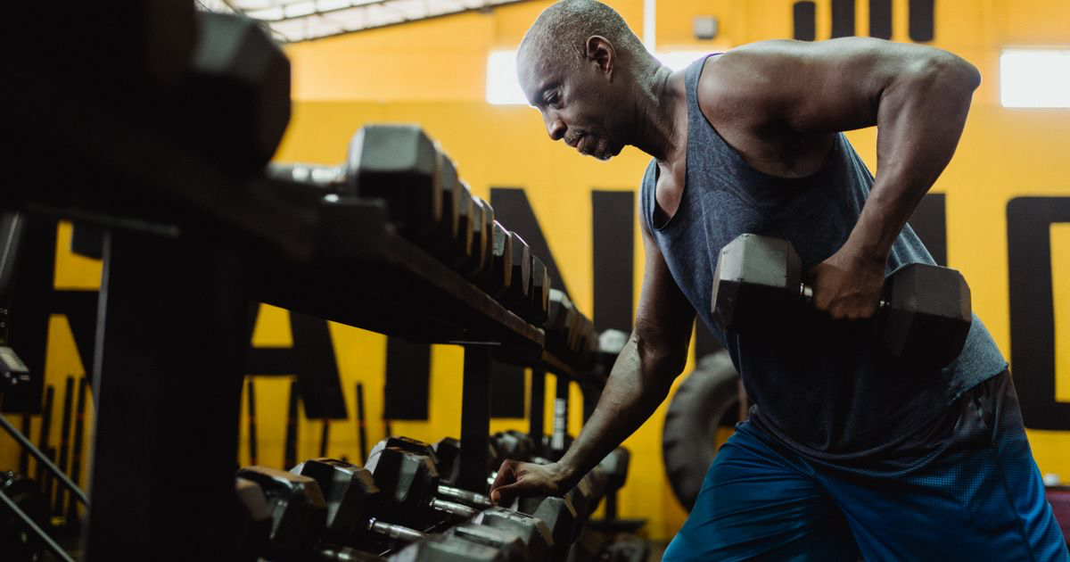 Man doing a one-arm dumbbell row with his free hand braced on a dumbbell rack