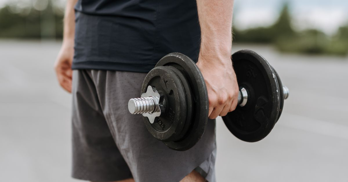 Man carrying a heavy dumbbell in one hand, demonstrating the farmer's walk exercise