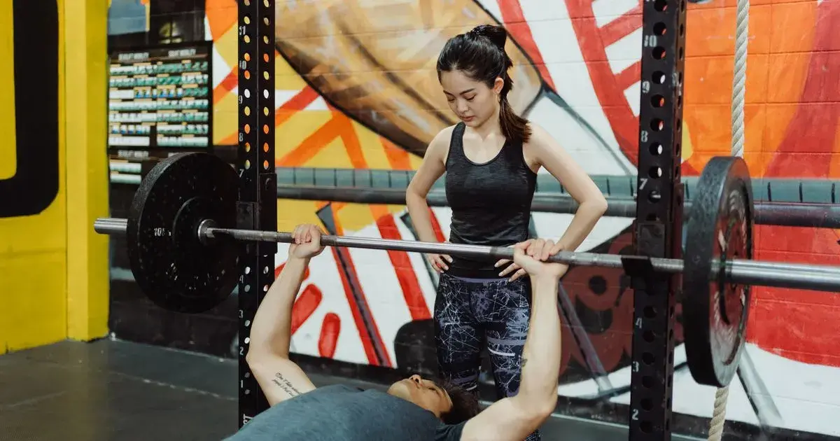 Spotter standing at the head of the bench while a lifter does a barbell bench press in a power rack
