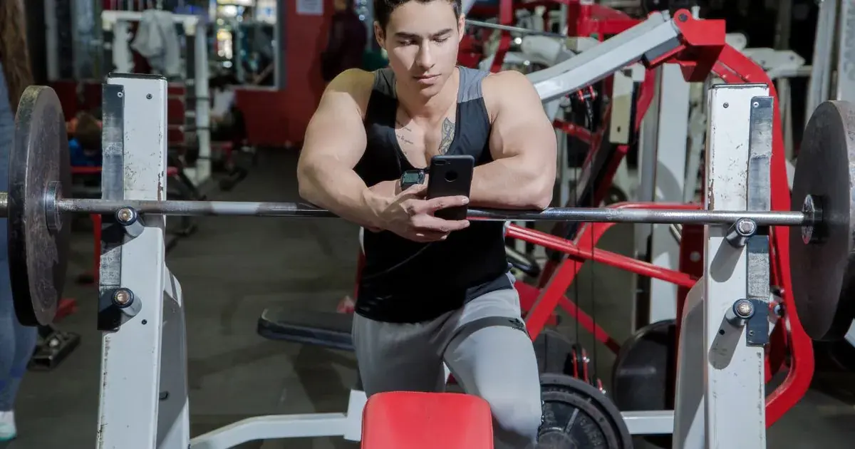 Lifter leaning on a barbell using his phone to track gym progress between sets