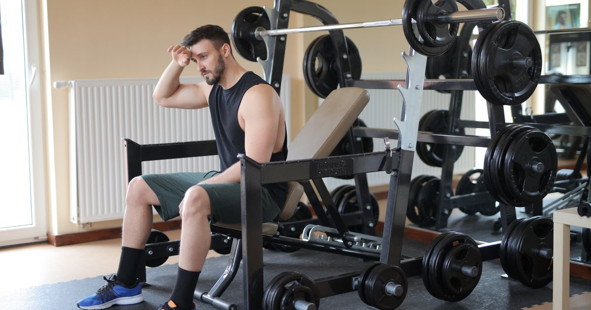 Lifter sitting on a gym bench looking mentally drained before a set, the scenario tested in mental fatigue and lifting performance research