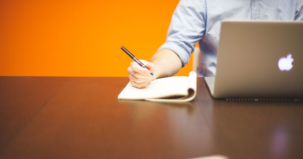 Person writing in a notebook beside a laptop, illustrating a Microsoft Word workout log template