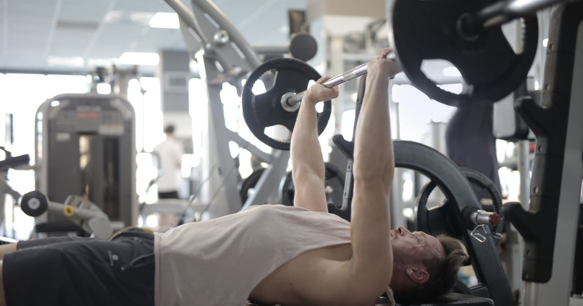 Lifter pressing a heavy barbell on a bench, the exercise used to test rest-pause vs drop sets
