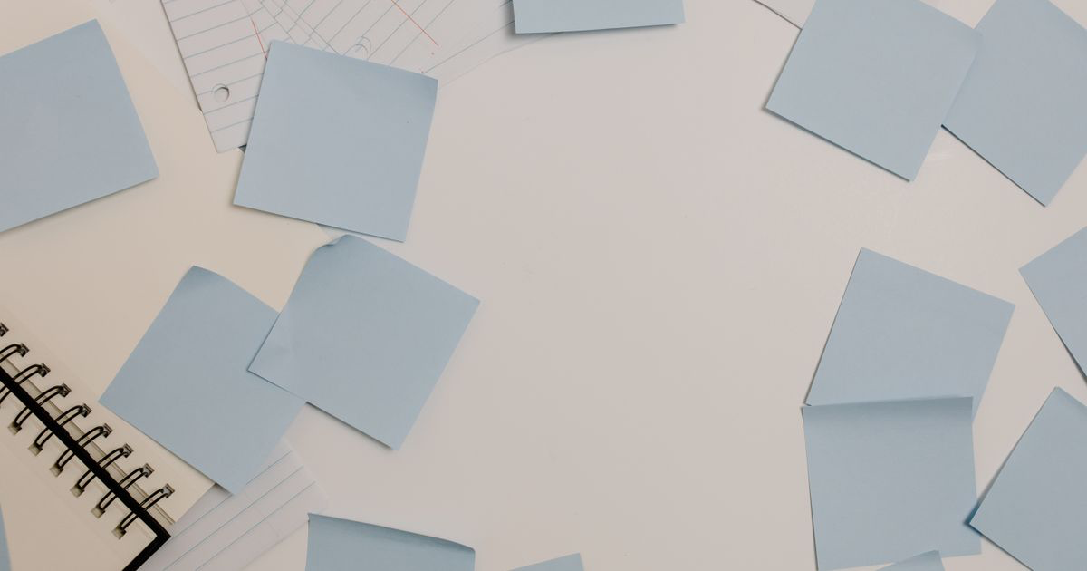 Sticky notes and a notepad scattered on a white desk, illustrating Strong app note vs sticky note