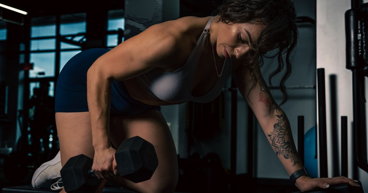 Woman performing a single-arm dumbbell lift in a gym, the unilateral vs bilateral training question tested in a 2026 study