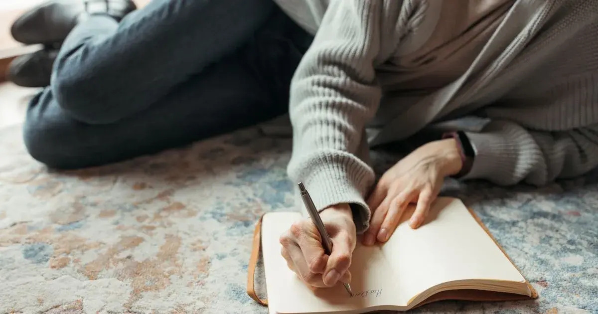 A lifter writing in a workout journal template with a fitness band on their wrist