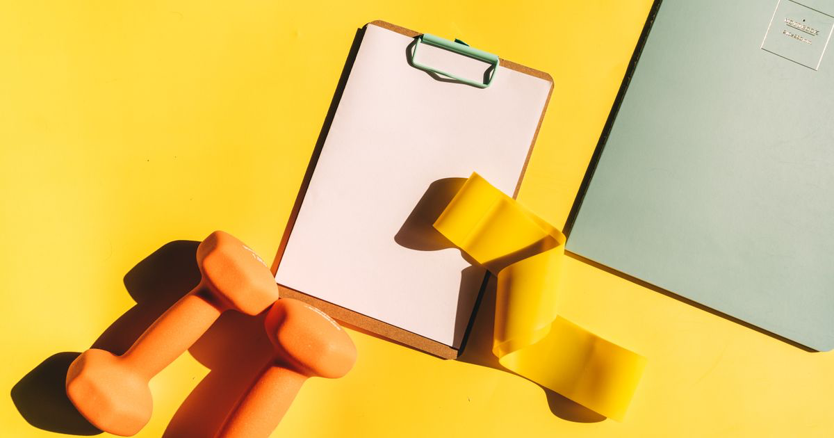 Workout log template on a clipboard beside dumbbells and a notebook